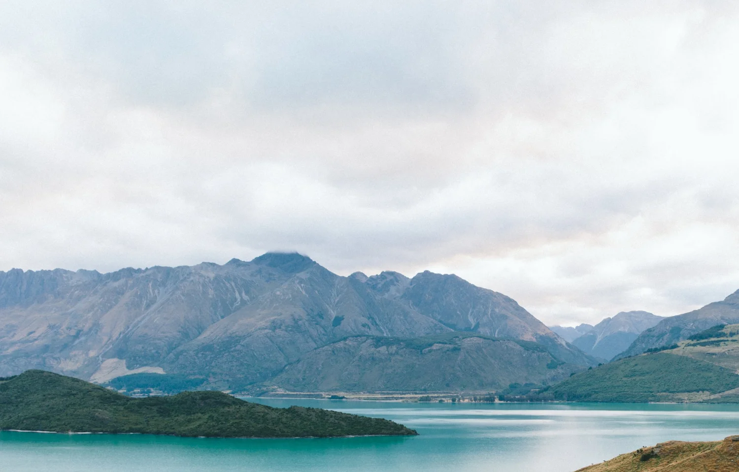 Scenic landscape with mountain range, lake, and cloudy sky during daytime.