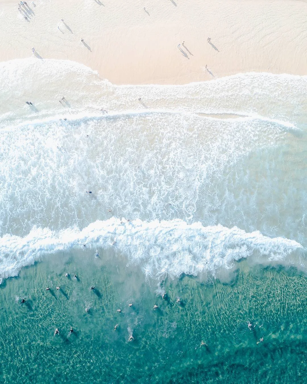 Aerial view of a beach with sand and ocean waves, with people swimming and walking along the shoreline. International English church in Seoul